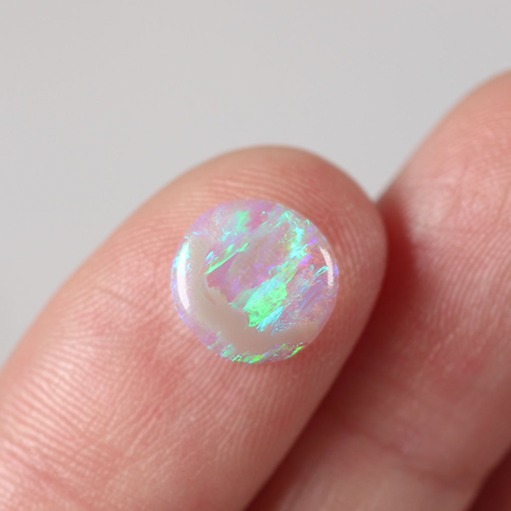 Light crystal opal held between fingers for size reference