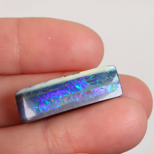 Boulder opal held between fingers for size reference