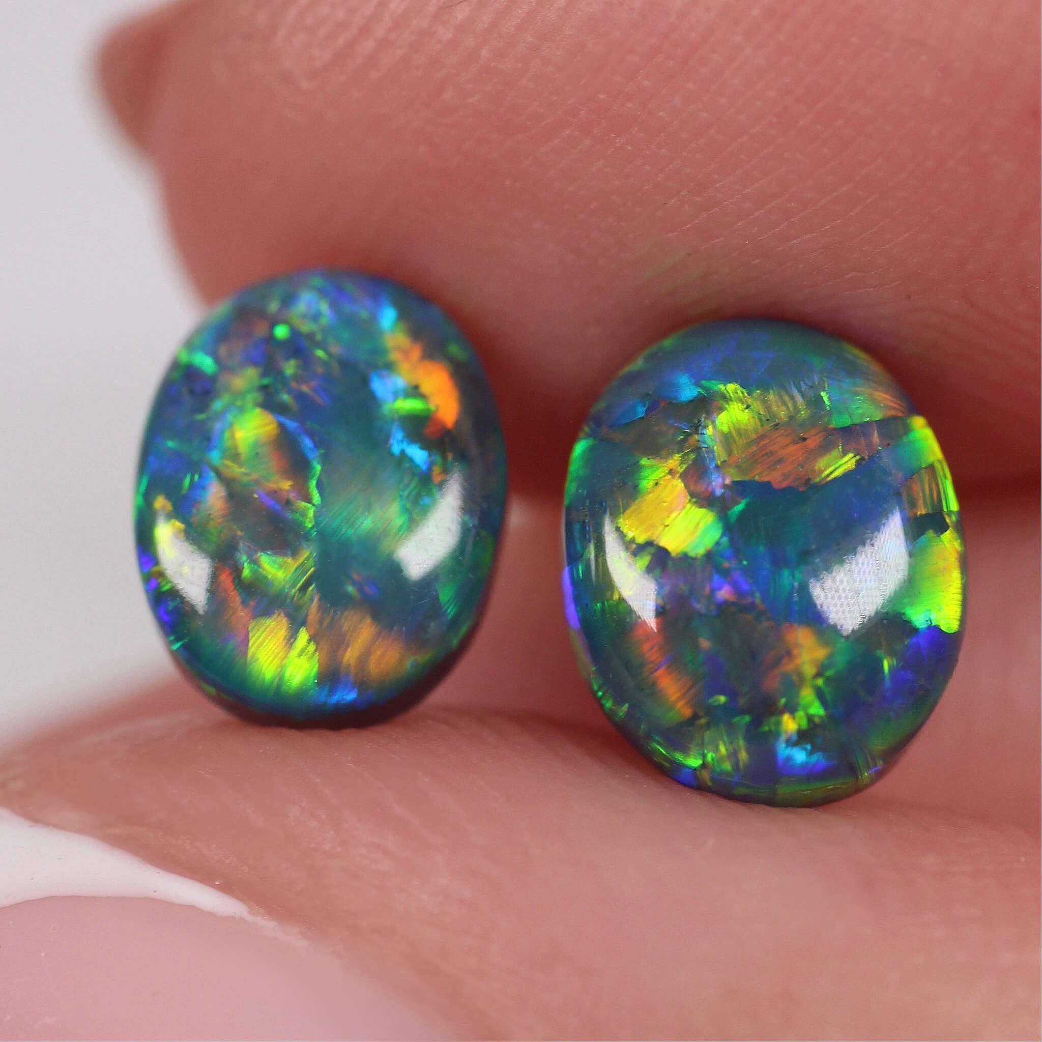 Two colorful opals held between fingers against a neutral background