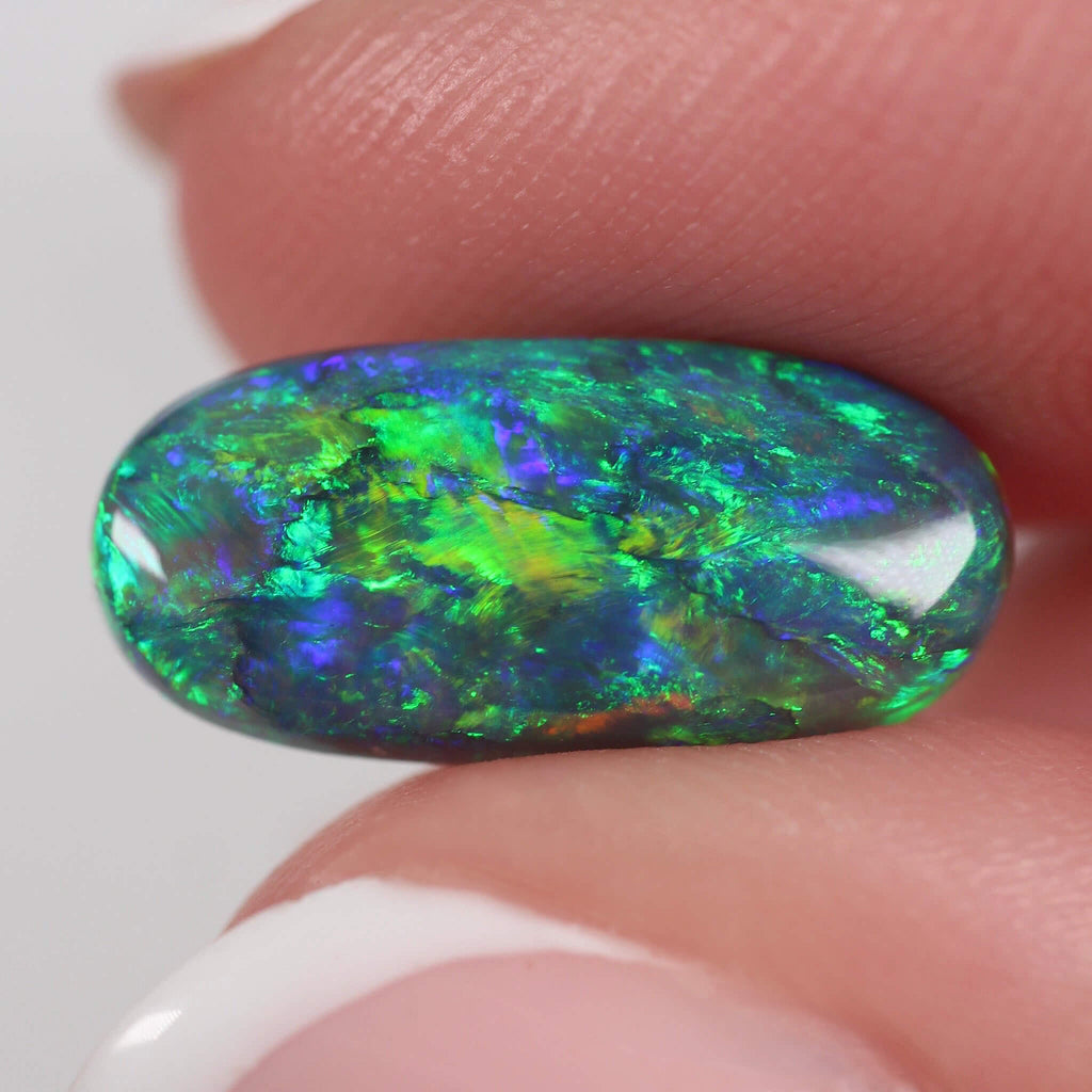 Multicolored opal stone held between fingers against a neutral background