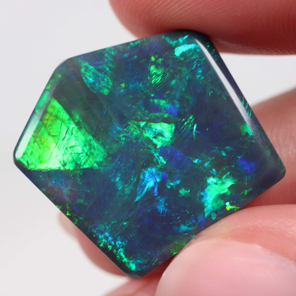 Hexagonal opal stone held between fingers against a white background