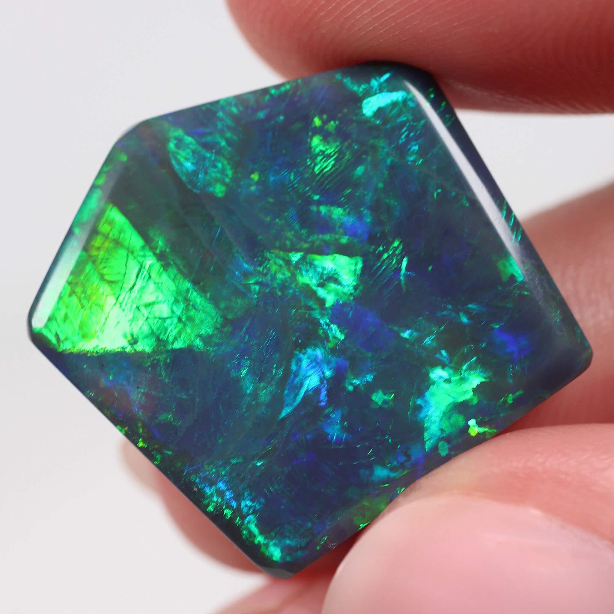 Hexagonal opal stone held between fingers against a white background