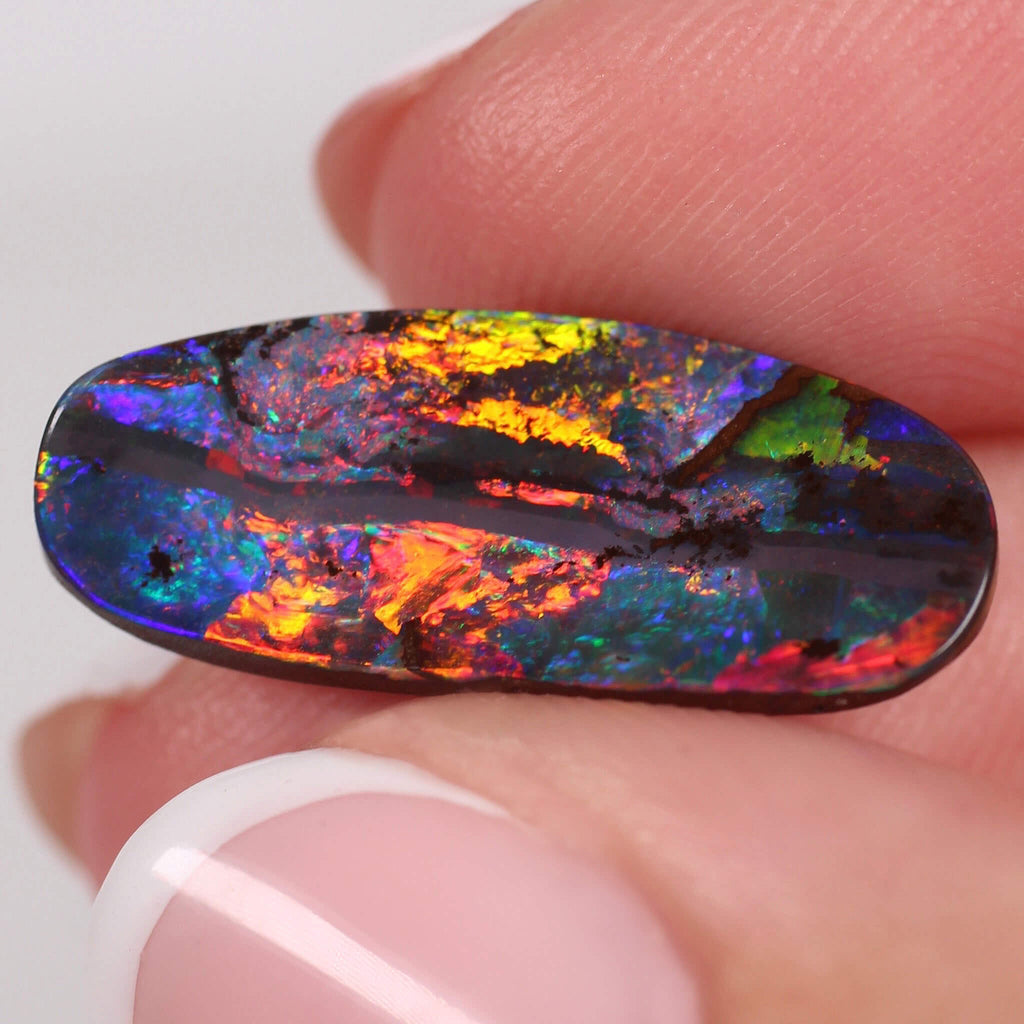 Multicolored opal stone held between fingers against a white background