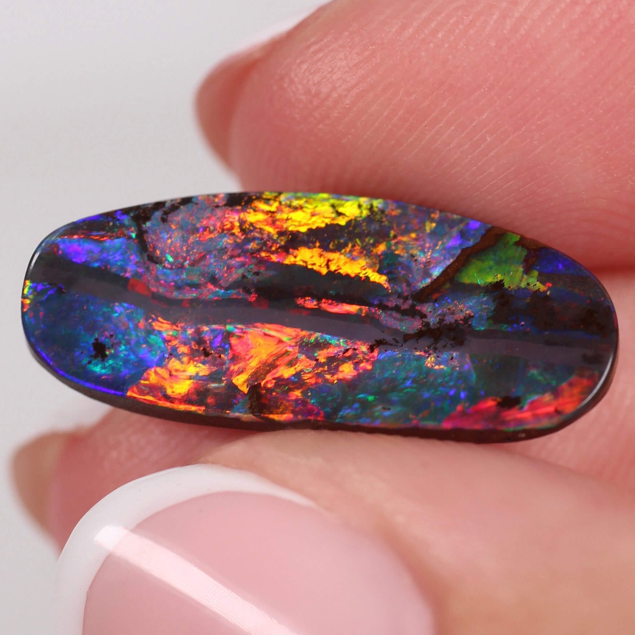 Multicolored opal stone held between fingers against a white background