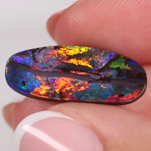Multicolored opal stone held between fingers against a white background