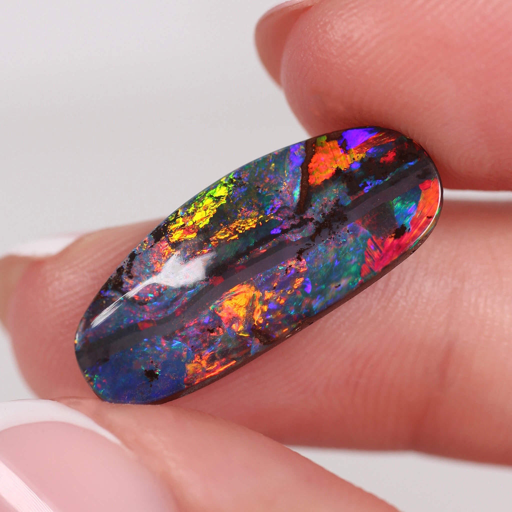 Multicolored opal stone held between fingers against a white background