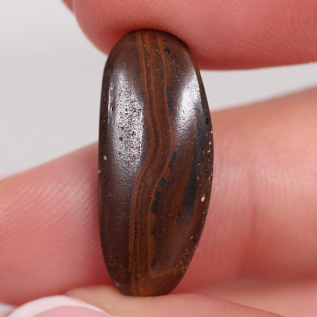 Brown stone with striped pattern held between fingers against a white background