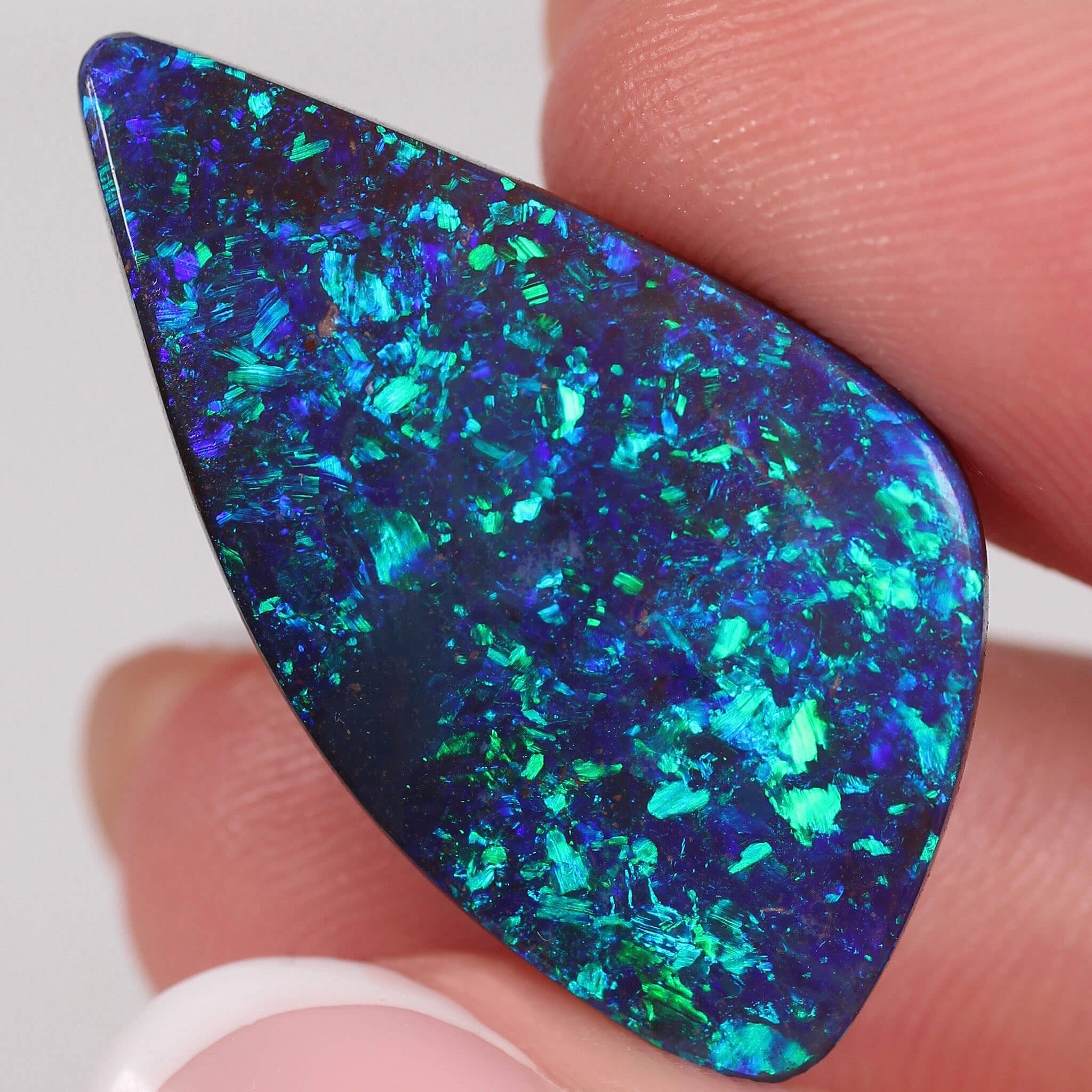 Close-up of a blue and green opal stone held between fingers.