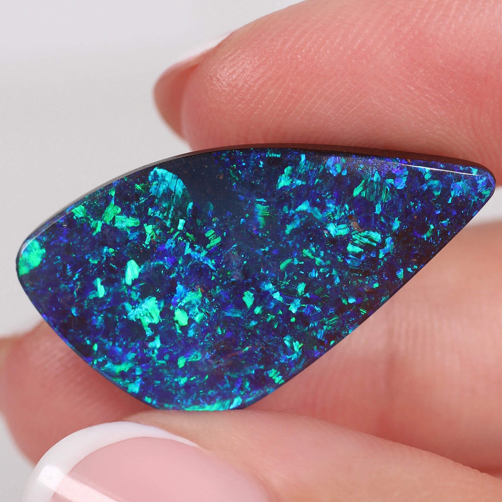 Blue green gem Opal stone held between fingers with a white background