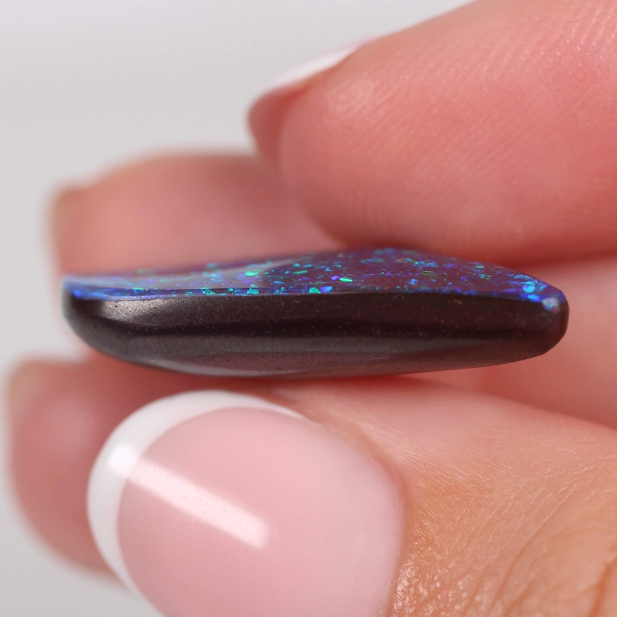 Opal stone held between fingers with a white background