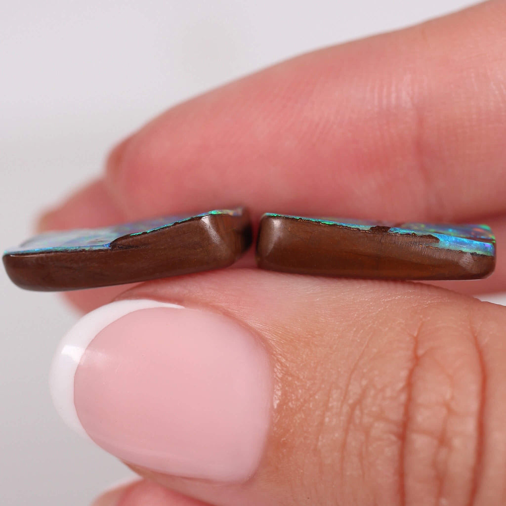 Close-up of two brown opal stones held between fingers against a white background