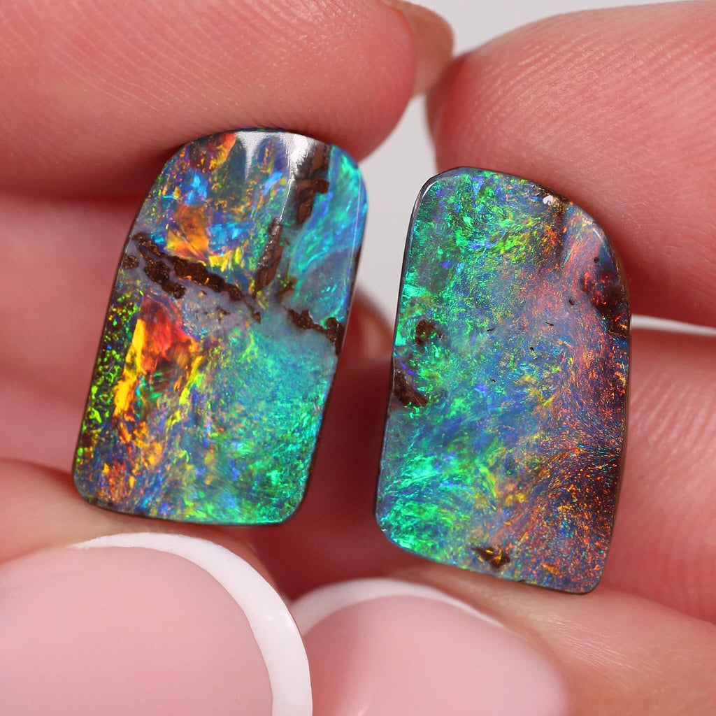 Two colourful boulder opal stones held between fingers against a neutral background