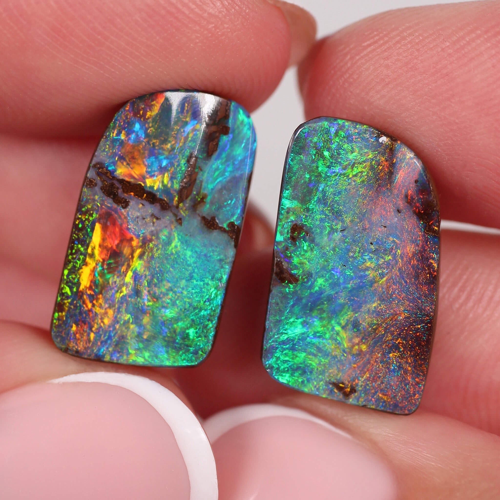 Two colourful boulder opal stones held between fingers against a neutral background