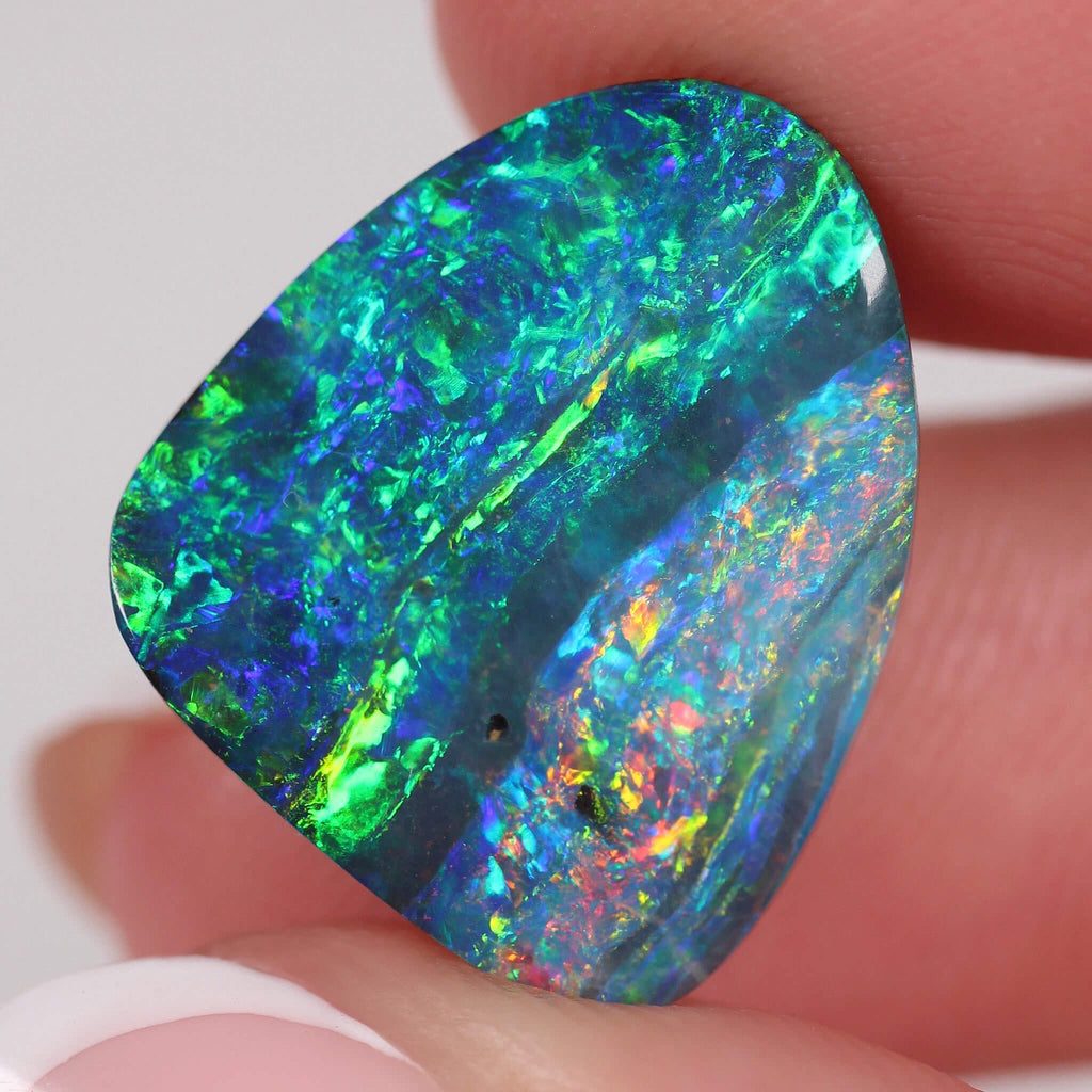 Multicolored opal stone held between fingers against a white background