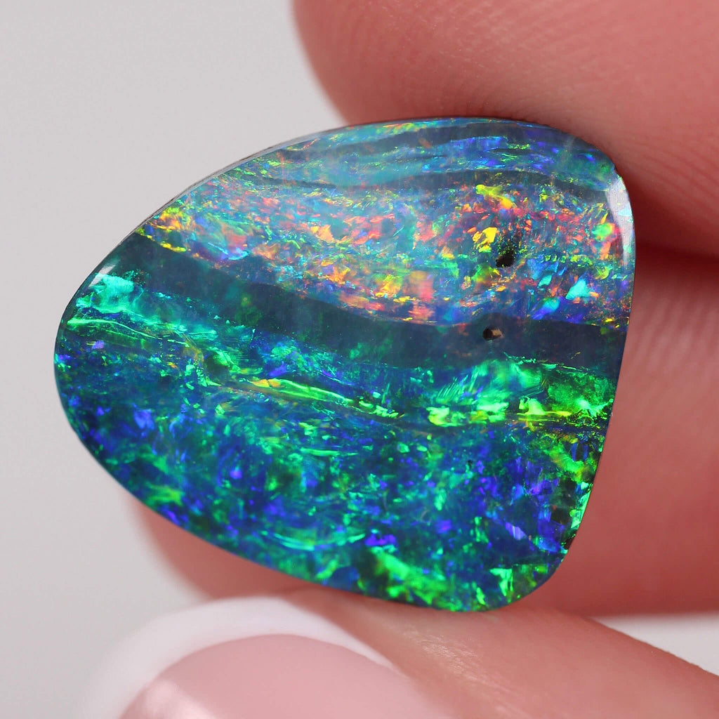 Multicolored opal stone held between fingers against a neutral background