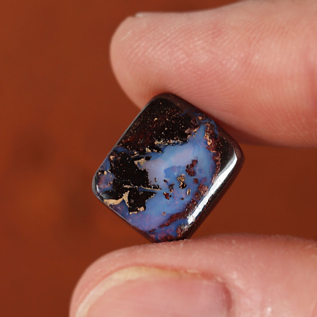 Boulder opal held between fingers for size reference